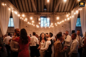 A vibrant and festive photo captured at Calke Abbey Riding School, featuring a joyous bride and groom dancing surrounded by their wedding guests in a rustic venue setting.